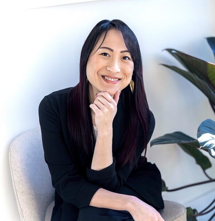 headshot of clinical psychologist wearing a black outfit sits on a chair with a hand resting on their chin and the other on their lap. located in a therapy office offering in-person therapy for individuals and couples in new york, midtown manhattan and brooklyn. Trauma-Informed Individual and Couples Therapy in NY